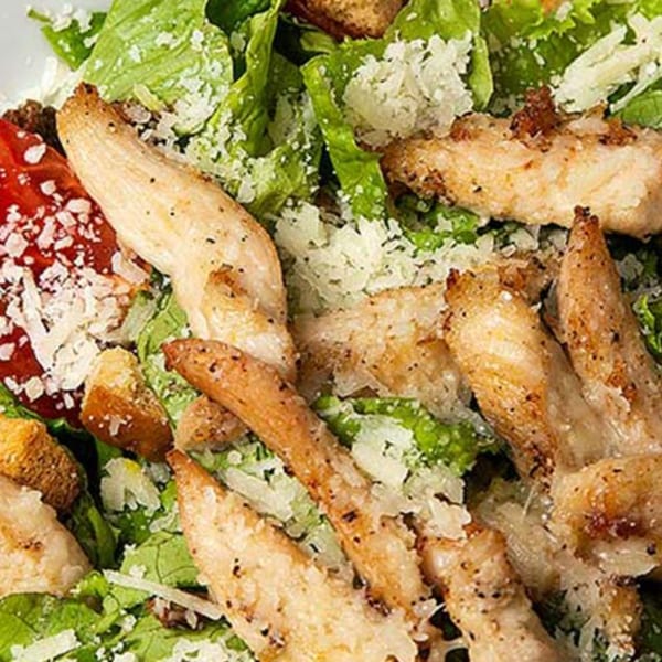 Close-up of a Caesar salad with grilled chicken strips, croutons, and grated cheese.