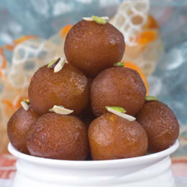 A white bowl filled with gulab jamun, garnished with slivered almonds and pistachios.