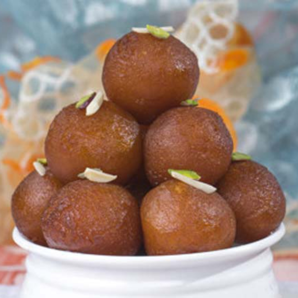 A white bowl filled with gulab jamun, garnished with slivered almonds and pistachios.