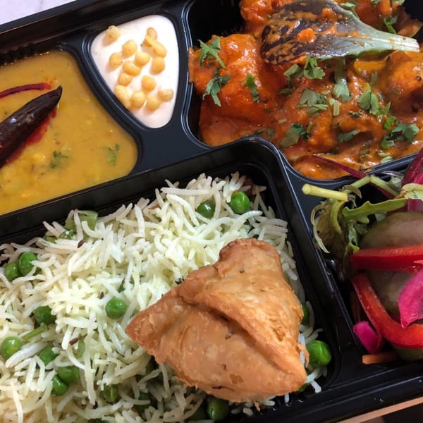 A Dakshin Indian Bistro takeout meal with butter chicken, dal, rice, samosa, raita, and salad.