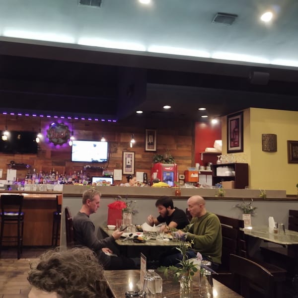 Diners seated at tables in a dimly lit Dakshin Indian Bistro, with a bar in the background.