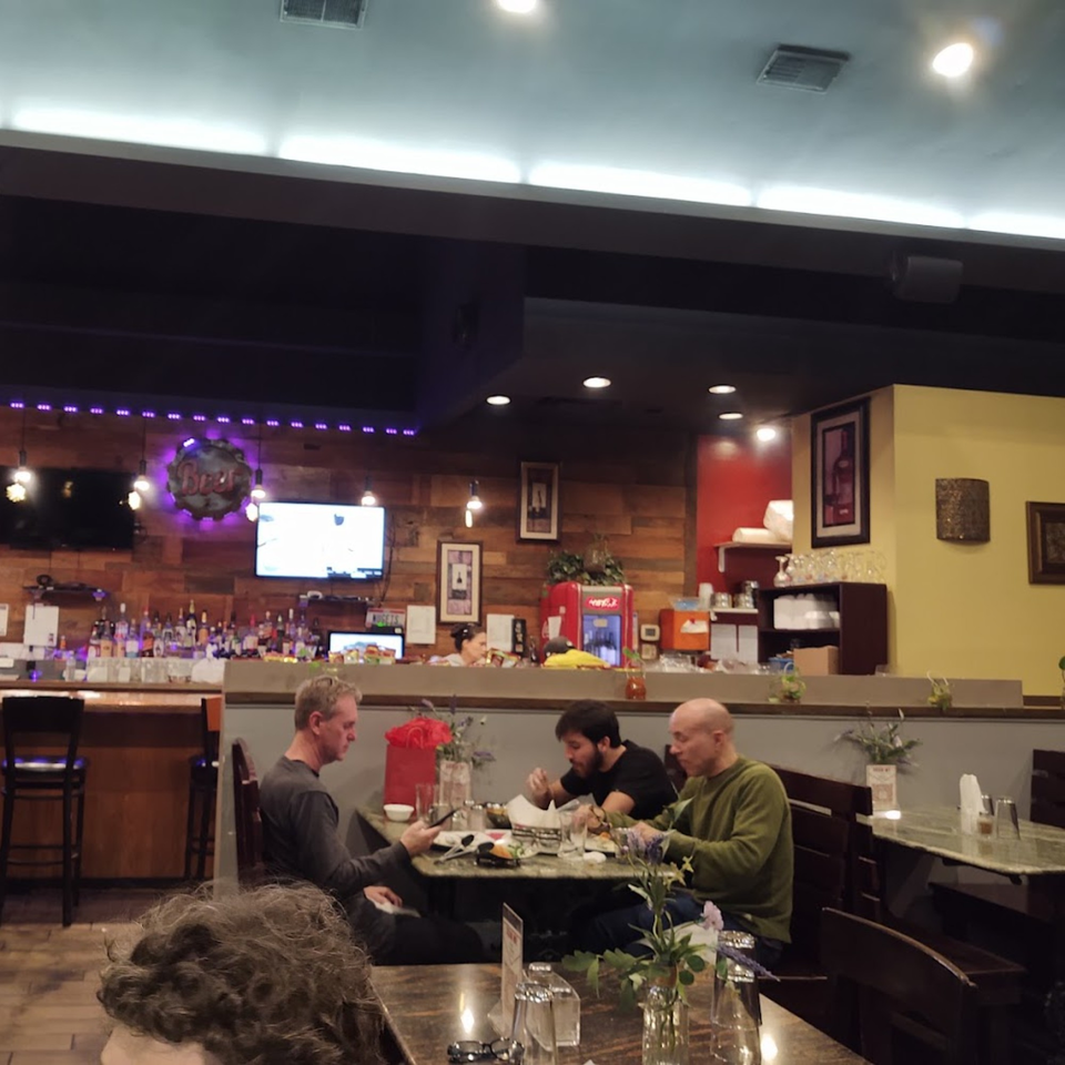 Diners seated at tables in a dimly lit Dakshin Indian Bistro, with a bar in the background.