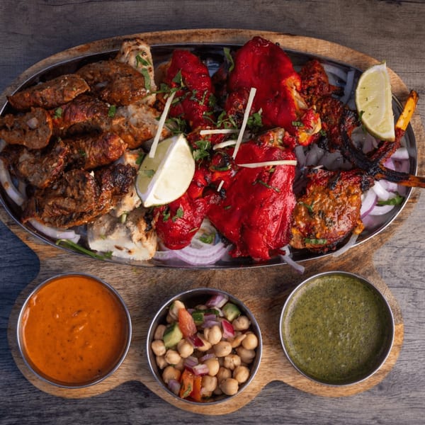 A large platter of various Indian grilled meats, including red tandoori chicken, with three dipping sauces.