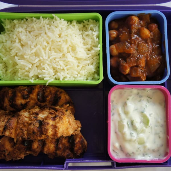 Indian bento box with rice, chana masala, grilled chicken, and raita.