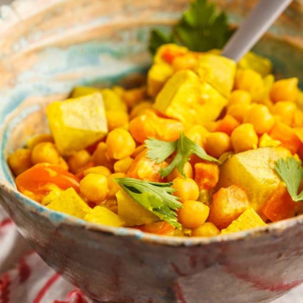 Close-up of a colorful Indian curry with chickpeas, paneer, and vegetables in a rustic bowl.