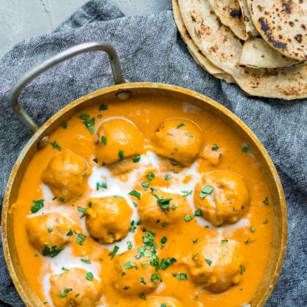 Indian malai kofta in a rich orange sauce with cream and cilantro, served with flatbread.