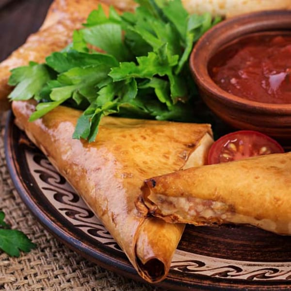 Crispy golden spring rolls with fresh parsley, a slice of tomato, and a bowl of red sauce.
