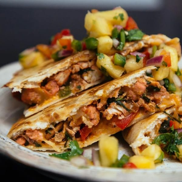 Indian chicken quesadillas topped with pineapple salsa, red onions, and cilantro on a white plate.