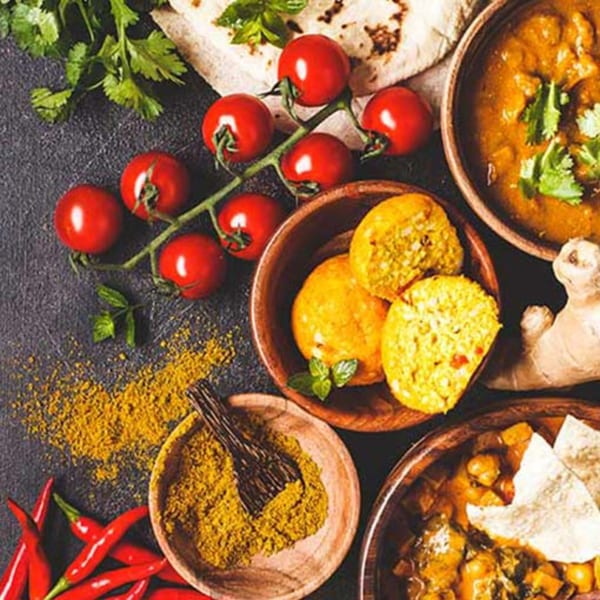 Indian dishes and ingredients, including curry, spices, tomatoes, chilies, and flatbread, on a dark surface.