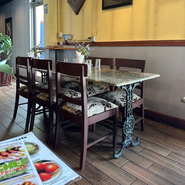 An empty dining table with four chairs and a menu on a wooden floor at Dakshin Indian Bistro.