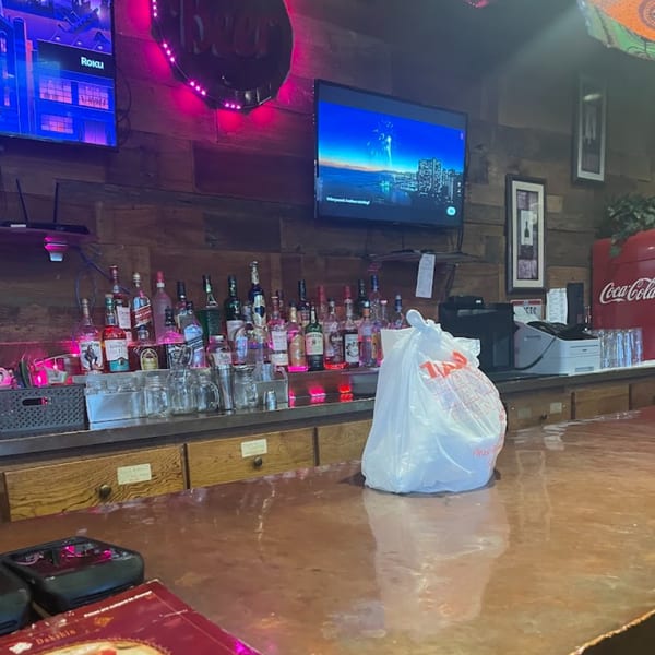 A bar area with liquor bottles, two TVs, and a white plastic bag on the counter.