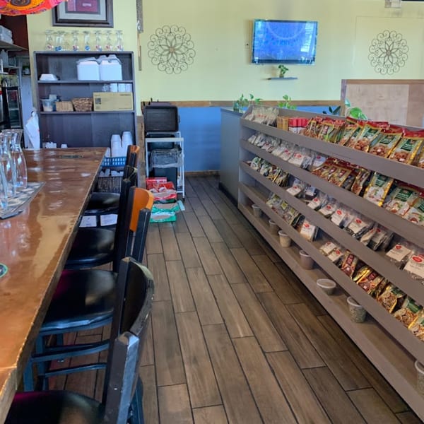 Interior view of Dakshin Indian Bistro, showing a bar, chairs, and shelves stocked with packaged goods.